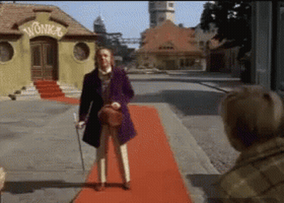 Man In Purple Coat On Red Carpet In Front Of Wonka Building GIF
