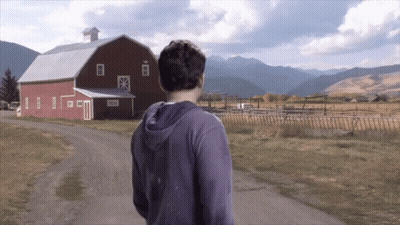 Man In Purple Hoodie Walking Past Red Barn GIF