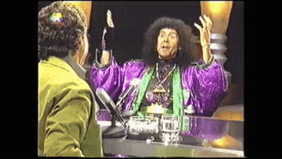 Man In Purple Robe Talking At Table With Microphone GIF