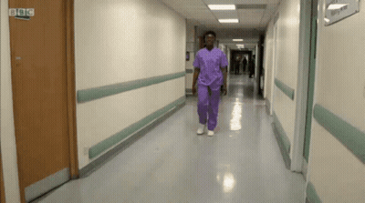 Man in Purple Scrubs Walking Past BBC Logo Door