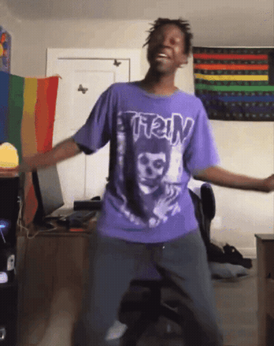 Man In Purple Shirt Dancing In Front Of Rainbow Flag GIF
