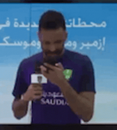 Man In Purple Shirt Holding Phone In Front Of TV GIF