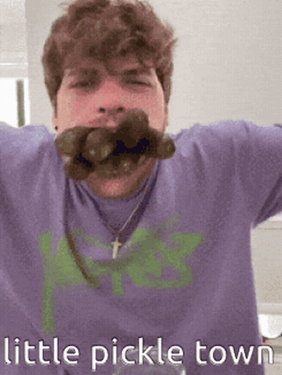 Man In Purple Shirt Holding Pickle In Mouth GIF