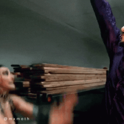 Man In Purple Shirt Holding Pile Of Wood GIF