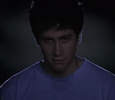 Man In Purple Shirt Looking At Camera In Dark GIF