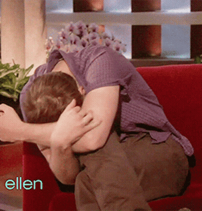 Man In Purple Shirt Sitting On Red Couch With Ellen Behind Him GIF