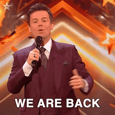 Man in Purple Suit Holding Microphone Saying We Are Back