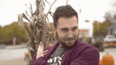 Man In Purple Sweater Standing Before Corn Stalks GIF