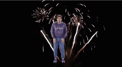 Man In Purple Sweatshirt Jumping In Front Of Fireworks GIF