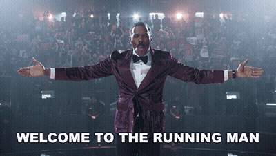 Man In Purple Tuxedo Saying Welcome To The Running Man GIF