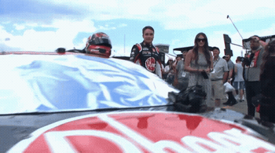 Man In Race Car Standing Next To Woman In Dress GIF