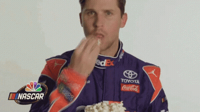 Man In Racing Suit Eating Popcorn From Cup GIF