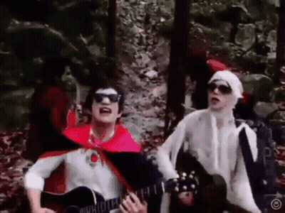 Man In Red Cape Playing Guitar Next To Man GIF