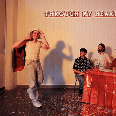 Man in Red Cape Stands Before Wall Saying Through My Heart