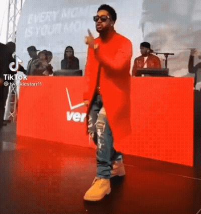 Man In Red Coat On Stage In Front Of Verizon Sign GIF