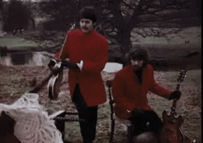 Man In Red Coat Playing Tambourine And Man On Chair Playing Guitar GIF