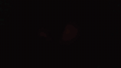 Man In Red Coat Staring At Camera In Dark Room GIF