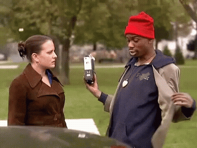 Man In Red Hat Holding Cell Phone In Front Of Woman In Brown Coat GIF
