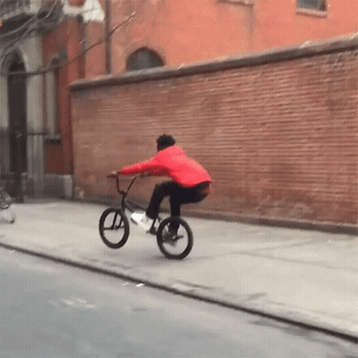 Man In Red Jacket Riding Bike Down Street GIF