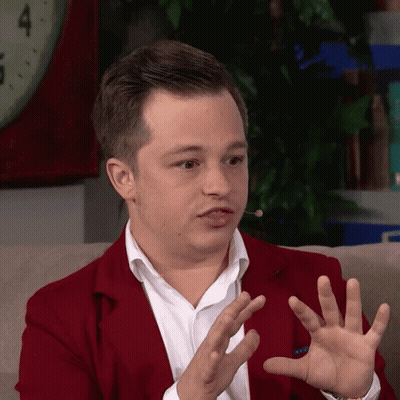 Man In Red Jacket Sitting On Couch With Hands Outstretched GIF