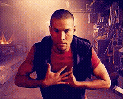 Man In Red Shirt And Black Vest Standing In Dark Room GIF