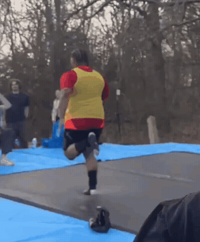 Man In Red Shirt And Yellow Vest Jumping On Trampoline GIF