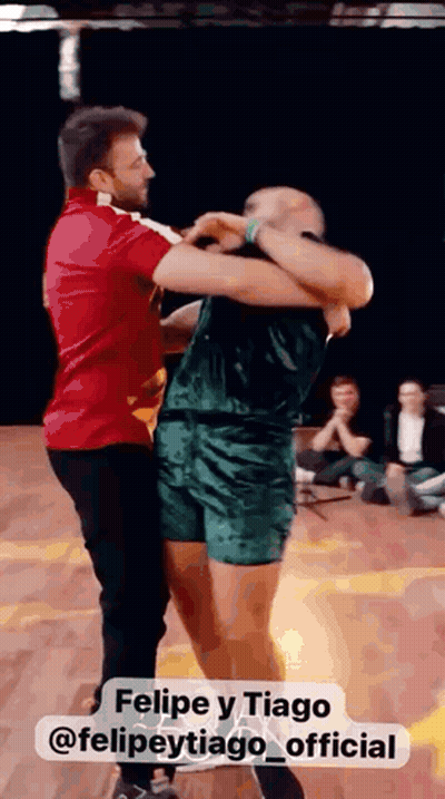 Man In Red Shirt Holding Man In Green Shorts Dancing GIF