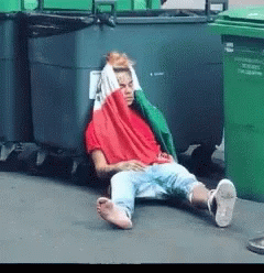 Man In Red Shirt Lying By Trash Cans GIF