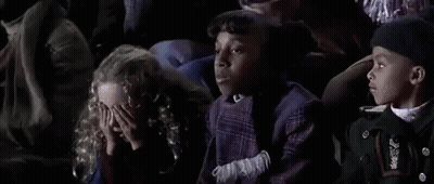 Man In Red Shirt On Cell Phone With Football Players Behind Him GIF