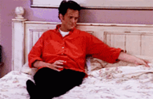 Man In Red Shirt Sitting On Bed Holding Beer GIF