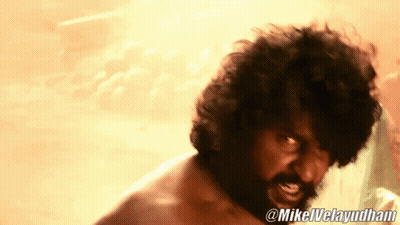 Man In Red Shirt Standing In Front Of Thatched Roof Building And Siriallu Sign GIF