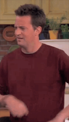 Man In Red Shirt Standing In Kitchen Making Funny Face GIF
