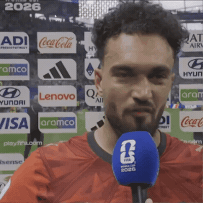 Man In Red Shirt Talking Into Blue Microphone With FIFA 2026 Logo GIF
