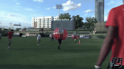 Man In Red Shirt Walking Past Ball Park Sign GIF