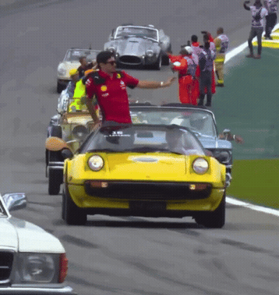 Man In Red Shirt Waves To Yellow Car On Track GIF