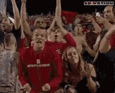 Man In Red Shirt With Letter S Surrounded By People GIF
