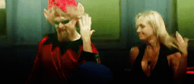 Man In Red Suit Next To Woman In Black Dress GIF