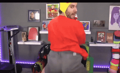 Man In Red Sweater And Yellow Hat Standing In Room With Pictures GIF