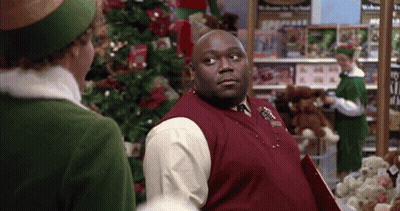 Man In Red Vest Next To Woman In Green Hat In Front Of Christmas Tree GIF