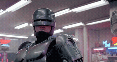 Man In Robot Costume In Front Of Bull Sign GIF