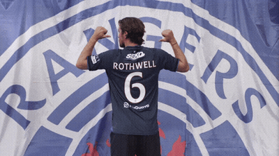 Man In Rothwell Jersey In Front Of Rangers Logo GIF