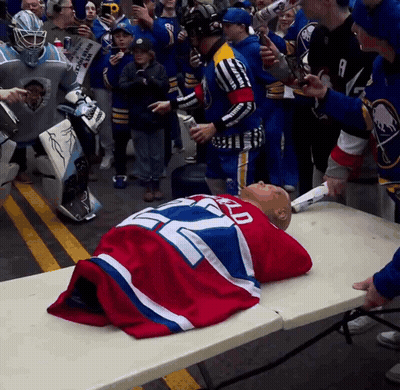 Man In Sabres Jersey Laying On Table Surrounded By Fans GIF