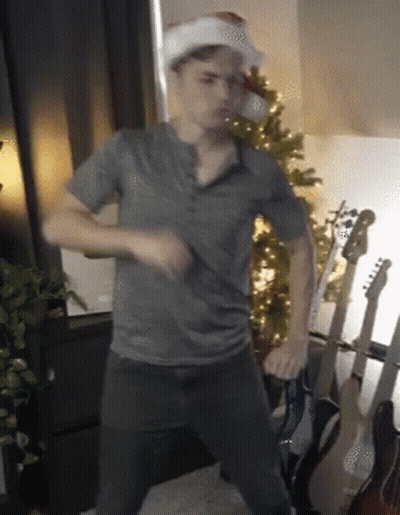 Man In Santa Hat Dancing By Christmas Tree GIF