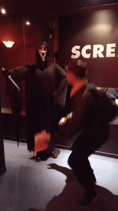 Man In Scream Costume Standing In Front Of Scream Sign GIF