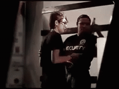 Man In Security Shirt Standing Next To Another Man GIF