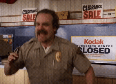 Man In Sheriff Uniform In Front Of Kodak Processing Center Sign GIF