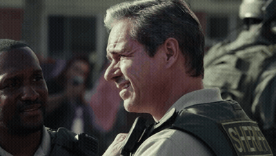 Man in Sheriff Vest Smiling Talking to Another Man