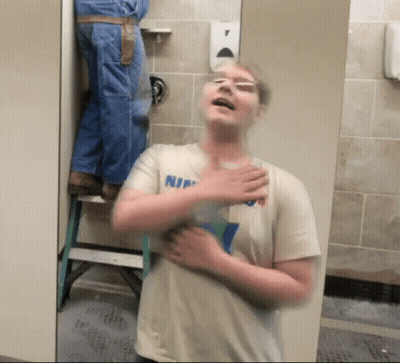 Man In Shirt Saying Nin Standing In Bathroom GIF