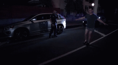Man In Shorts Standing In Front Of Police Car At Night GIF