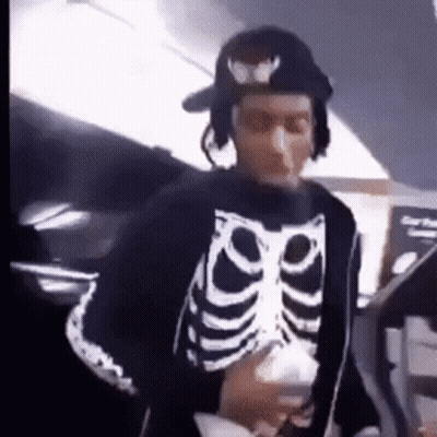 Man In Skeleton Sweater And Hat Holding Cup GIF